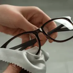 Dłoń czyści okulary brązową oprawką jasnoszarą ściereczką.