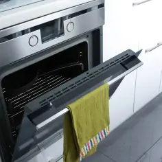 Otwarty piekarnik z funkcją **pyrolizy**, w środku kratka i forma. Na drzwiczkach wisi zielony ręcznik.
