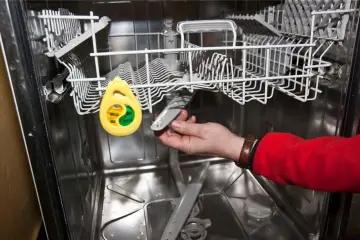 Ręka wkłada do zmywarki tabletkę, gdy ta nie domywa naczyń.